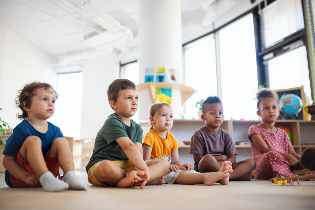 Five young children sitting in a row on the floor in a play learning space